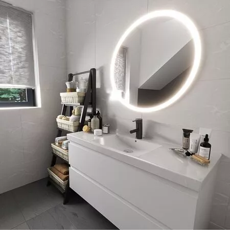 Modern Badezimmer mit ovalem Spiegel, Waschbecken und Regal für Pflegeprodukte.