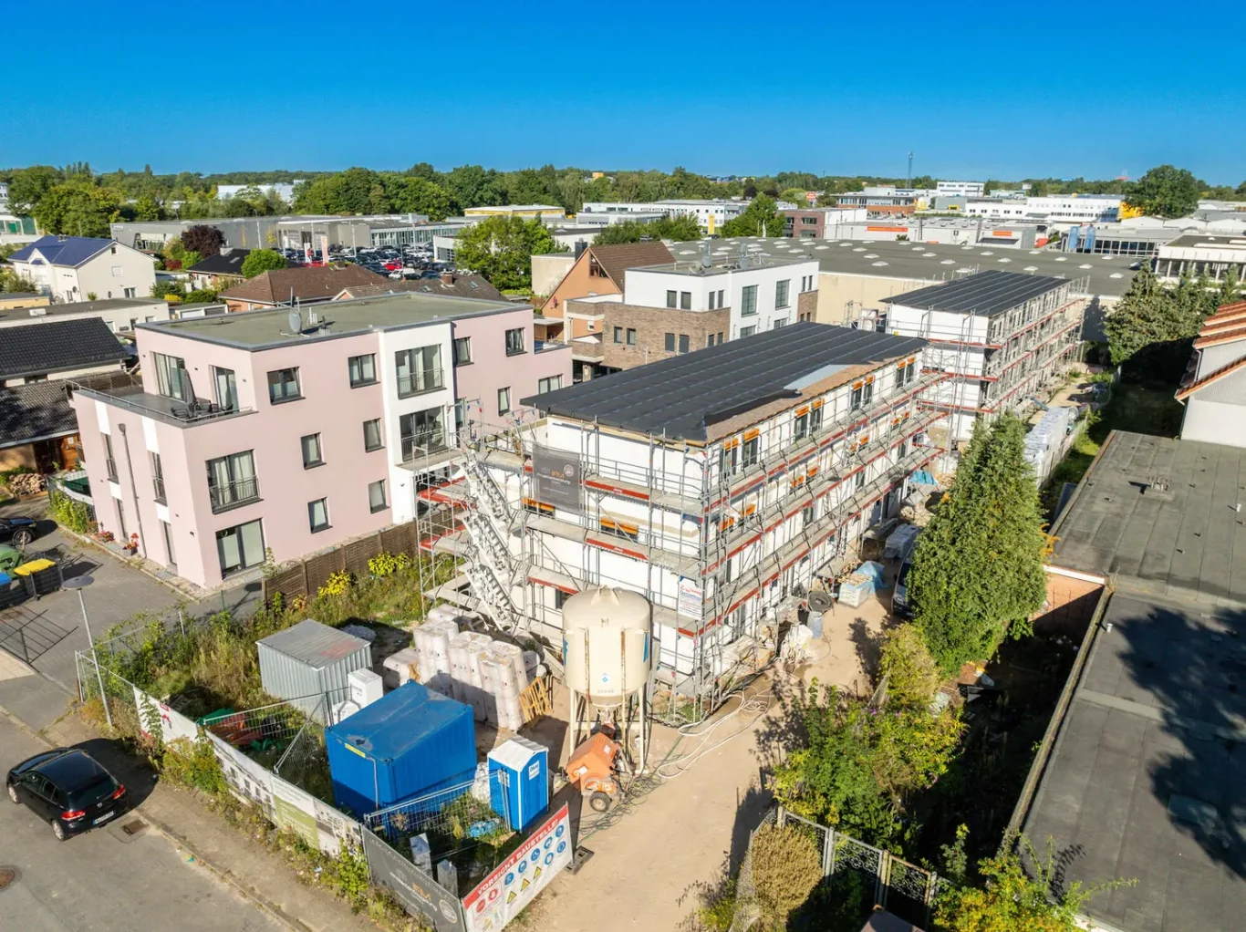 Baustelle mit mehreren Mehrfamilienhäusern und Industrieanlagen im Hintergrund.
